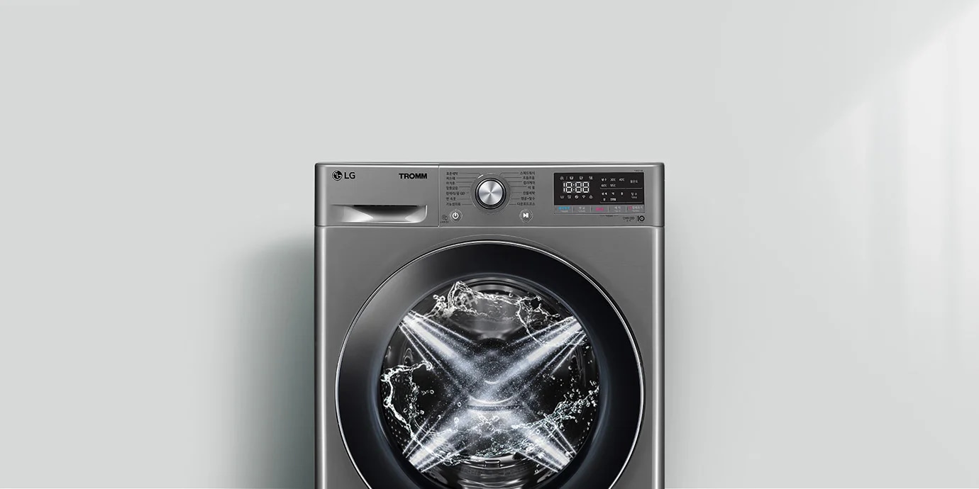 LG 트롬 세탁기가 보입니다. 세탁기 문 안쪽에는 물이 회전하며 세탁이 진행 중인 모습이 보입니다. 세탁기 상단에는 다양한 세탁 모드와 설정을 위한 다이얼과 디지털 디스플레이가 있습니다. 디스플레이에는 시간과 여러 설정 옵션이 표시되어 있습니다. 